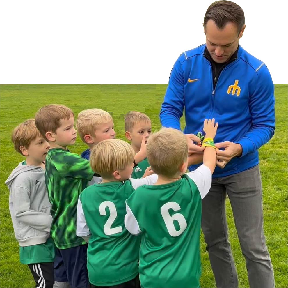 Soccer coach putting on wrist coach from Stumbling GOAT onto outreached arm of young boy