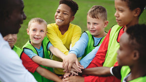 Youth boys soccer team stacking hands in huddle with smiling coach